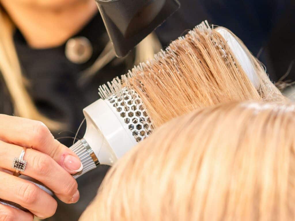 hair on wig being blow-waved with round brush
